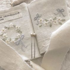 two white linens with embroidered flowers and ribbons on them, one is folded in half