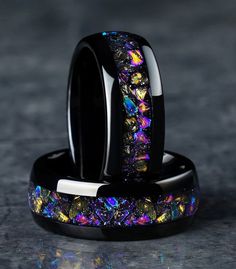 two black rings with colorful designs on them sitting next to each other in front of a dark background