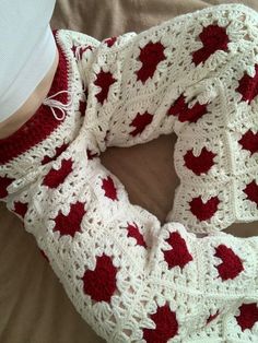 a crocheted red and white scarf on top of a bed next to a baby's leg