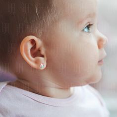 a close up of a baby's face with ear piercings on her ears