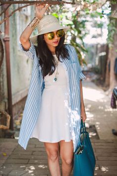 a woman in a white dress and hat carrying a blue bag