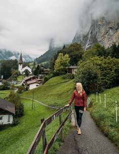 a woman is walking down a path in front of a mountain village with a church on it