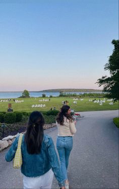 two women walking down the road in front of a lake