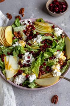 a salad with apples, cranberries and goat cheese in a bowl next to pecans