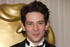 a man in a tuxedo and bow tie posing for the camera with an oscar statue behind him