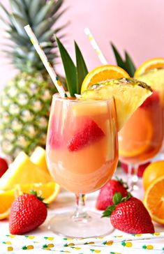 two glasses filled with lemonade and strawberries next to pineapples on a table