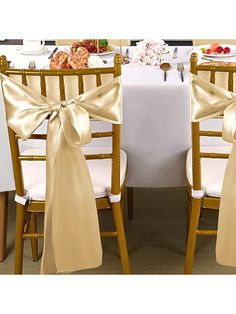 two chairs with bows tied around them at a table set up for a formal function