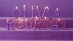 a purple cake with lit candles on it and the word roma written in cursive letters