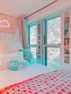 a white bed with pink and blue comforter next to two windows in a bedroom