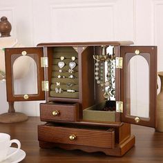 an open jewelry box sitting on top of a wooden table next to a cup and saucer