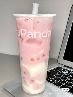 a pink drink sitting next to a laptop on a white table with the word panda written in it