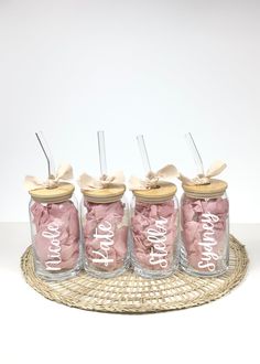 four pink mason jars with straws and bows on them sitting on a wicker tray