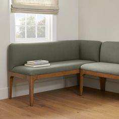 a corner bench with a book on it in front of a window and wooden floor