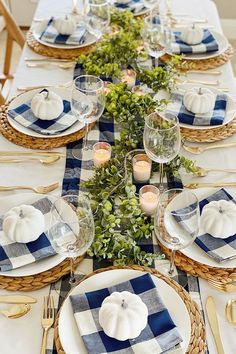 the table is set with blue and white plaid napkins, silverware, pumpkins and greenery