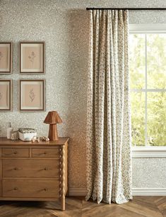 a room with a dresser, lamp and pictures on the wall above it in front of a window