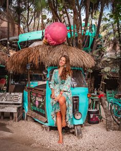 a woman sitting on the back of an old truck in front of a hut with thatched roof