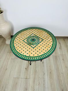 a green and yellow table sitting on top of a wooden floor next to a vase