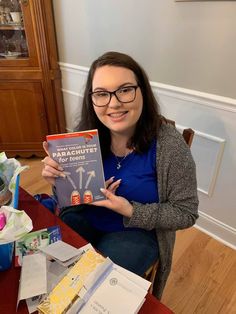 a woman sitting at a table holding up a book