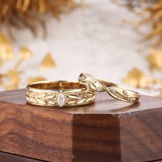 two gold wedding rings sitting on top of a wooden box next to a golden plant