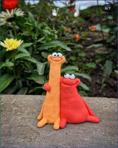 two clay animals sitting next to each other on top of a stone slab with flowers in the background