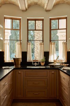 a kitchen with wooden cabinets and black counter tops in front of three large windows that look out onto the outdoors