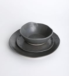 three black plates and one bowl on a white surface