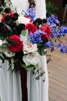 a woman in white dress holding a bouquet of flowers and greenery on her wedding day