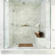 a walk in shower sitting next to a white tiled wall and floor with a vase filled with flowers on the side