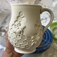 a hand holding a ceramic mug with bees and honeycombs on it