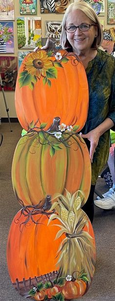 a woman standing next to a stack of pumpkins in an art room with paintings on the wall behind her