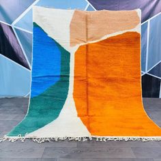 an orange, blue and green rug with fringes on the floor in front of a wall