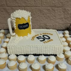 a beer mug sitting on top of a cake surrounded by cupcakes