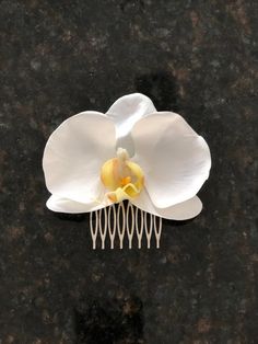 a white flower with yellow center sitting on top of a black table next to a hair comb