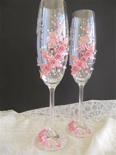 two wine glasses with pink flowers on them sitting on a lace doily covered table