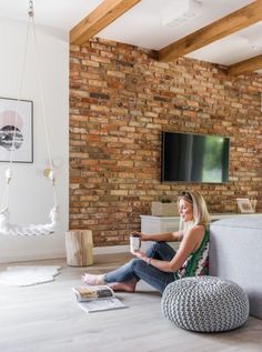 a woman sitting on the floor in front of a brick wall and holding a cup