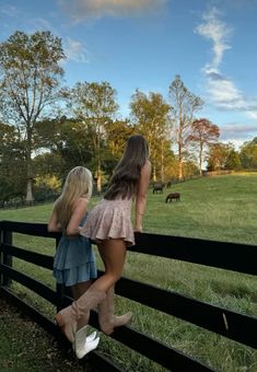 two girls looking over a fence at cows grazing in the field behind them on a sunny day