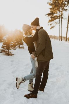 a man and woman standing in the snow with their arms around each other as they kiss