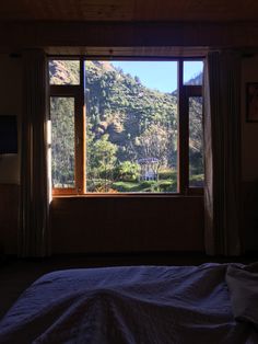 a bed sitting under a window next to a forest filled mountain side covered in trees