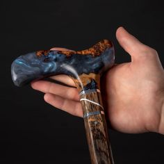 a hand holding a wooden object in it's right hand, with blue and brown swirls on the top