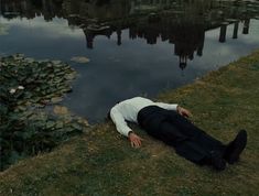 a man laying on the ground next to a body of water with lily pads in it