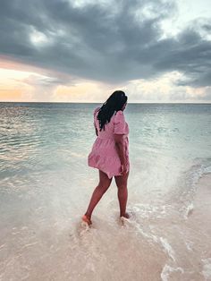 a woman standing in the water on top of a sandy beach next to the ocean