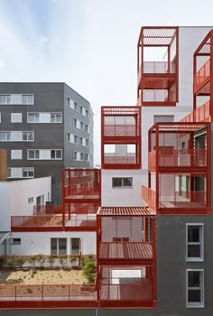 an apartment building with red balconies on the top and bottom floors, in front of other buildings