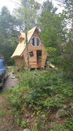 a small wooden cabin sitting in the woods next to a blue truck and some trees