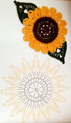 two crocheted sunflowers on a white surface with black and orange accents