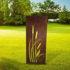 a tall wooden sign sitting on top of a lush green grass covered park field with trees in the background