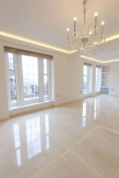 an empty living room with chandelier and large windows in the center, all white