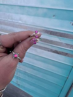 a person with pink and silver rings on their fingers next to a blue wall,