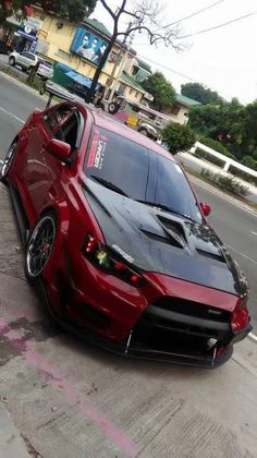 a red and black car parked on the side of a road next to a building