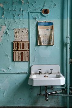 a bathroom with peeling paint on the walls and a sink in front of an old book shelf