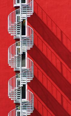 three white balconies on the side of a red building with shadows cast by them